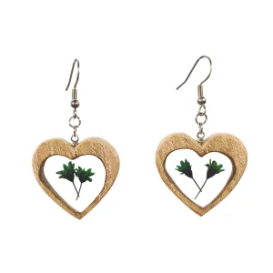 Par de brincos artesanais em madeira de olmo em forma de coração com folhas verdes encapsuladas em resina, pendentes com gancho prateado.