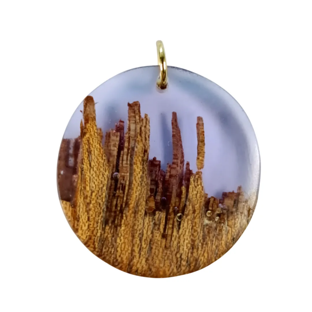 Circular pendant in acacia wood and translucent lilac resin, detailing the organic pattern of the wood.