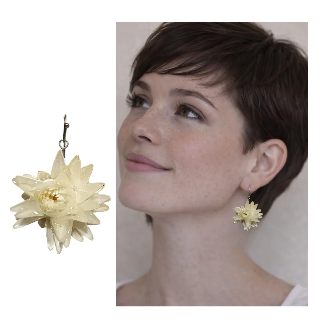 Model with short dark hair wearing a white natural flower earring in crystal resin, with an enlarged photo of the earring on the side.