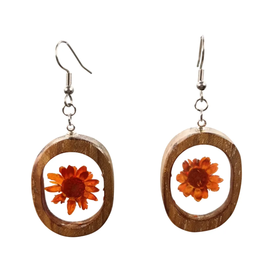 Par de brincos artesanais em madeira de acácia com flor laranja encapsulada em resina, pendente oval com gancho prateado.